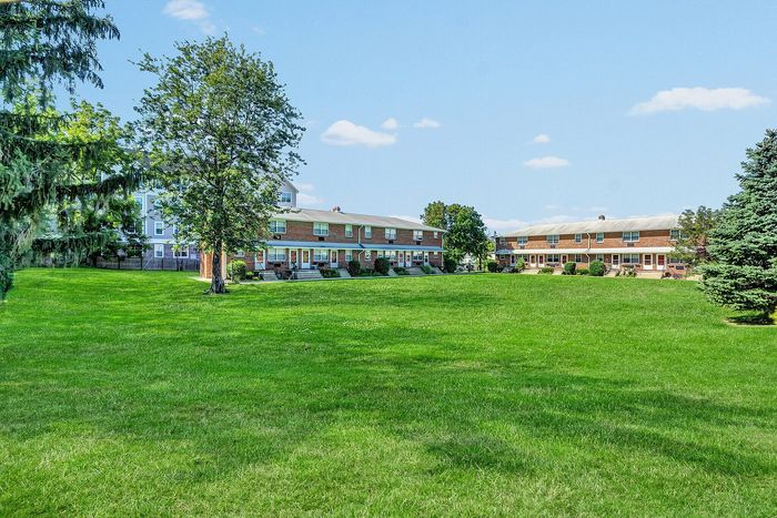 Charming brick apartments with lush green lawns and mature trees under a bright blue sky, perfect for peaceful living.