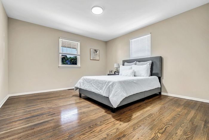 Bright and inviting bedroom with hardwood floors, featuring a plush gray bed and crisp white bedding against a backdrop of soft beige walls.