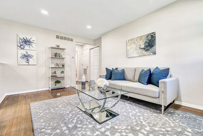 Elegant living room with a modern grey couch adorned with blue pillows, complemented by a sophisticated glass coffee table on a plush area rug and stylish artwork on the walls.