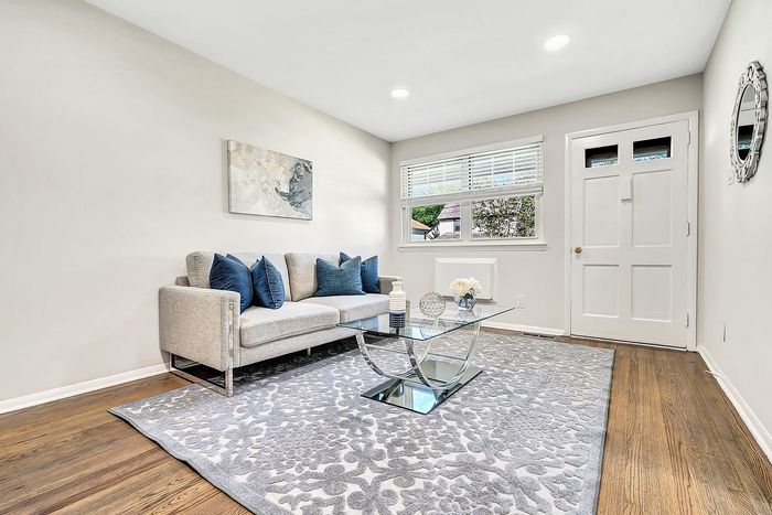 Charming living room with elegant gray sofa, plush blue pillows, and a modern glass coffee table atop a stylish patterned rug.
