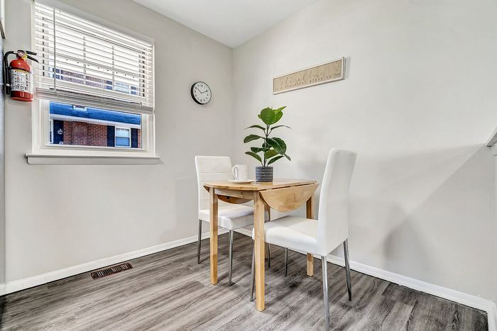 Charming dining nook with natural light, featuring a cozy wooden table, elegant white chairs, and a vibrant green plant for a welcoming atmosphere.
