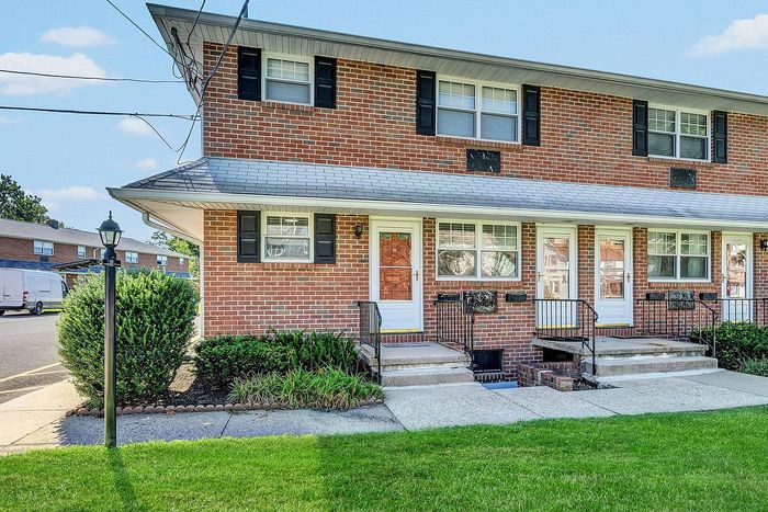 Charming brick townhouse with classic black shutters, welcoming front entrance, and tidy landscaping exuding suburban appeal.