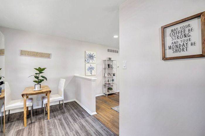 Inviting dining nook with modern decor, featuring a chic wooden table, white chairs, and a vibrant plant, seamlessly connected to a cozy living area with stylish shelving and decor.