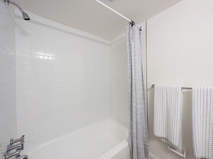 Bright and pristine bathroom with elegant white tile, a cozy bathtub, and stylish patterned towels enhancing a serene atmosphere.