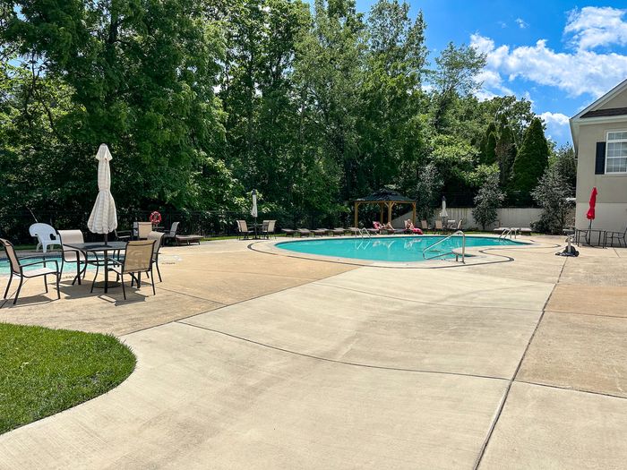 Inviting outdoor pool area with comfortable seating and lush greenery, perfect for relaxation and gatherings under blue skies.