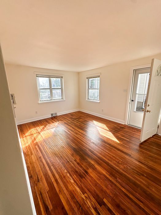 Bright room with gleaming hardwood floors, multiple windows, and abundant natural light creating a warm and inviting atmosphere.