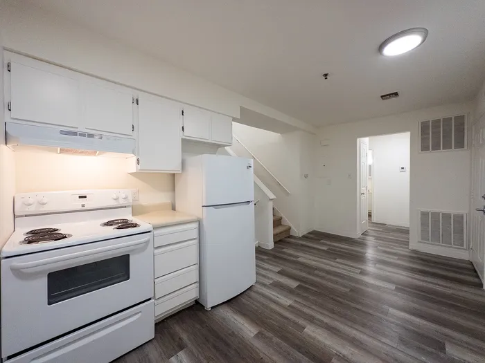 Modern kitchen with sleek white cabinetry, electric stove, and ample space, leading to a cozy staircase and well-lit interior.