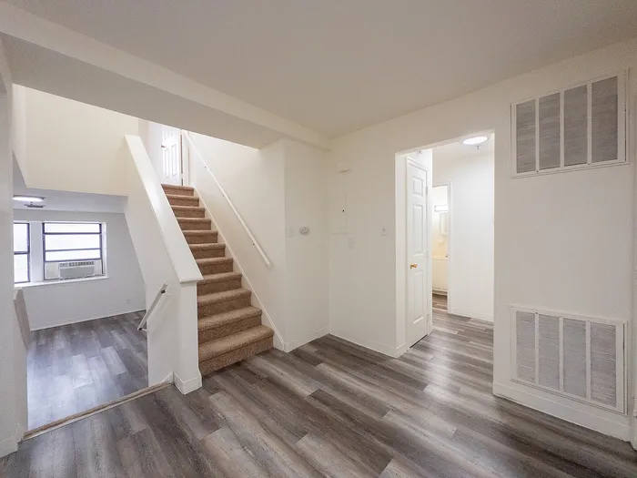 Bright and spacious apartment interior featuring modern flooring and a carpeted staircase leading to the upper level.