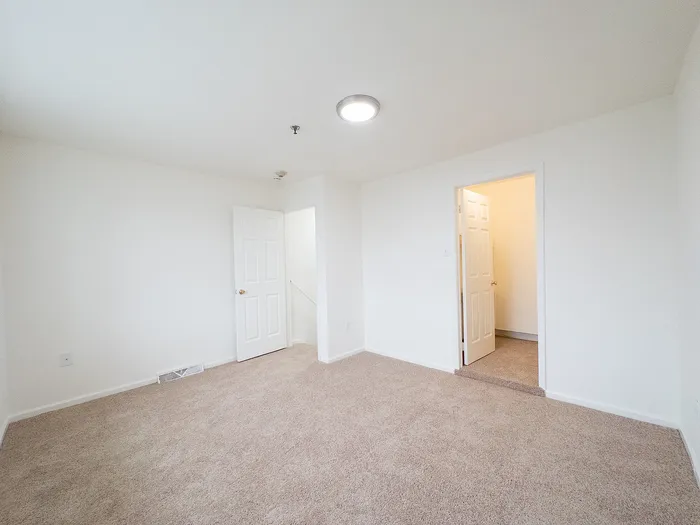 Spacious and bright carpeted room with clean white walls and two open doors, inviting natural light and warmth.