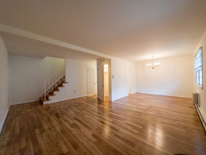 Spacious living area with elegant chandelier, hardwood floors, and convenient staircase leading upstairs, offering a perfect blend of charm and functionality.