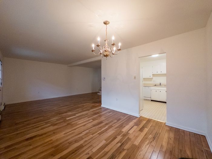 Inviting open-concept living space with elegant chandelier, showcasing polished wooden floors and a view into a cozy kitchen.