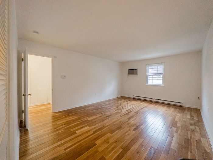 Bright and spacious room with elegant hardwood flooring and ample natural light from a sunlit window.