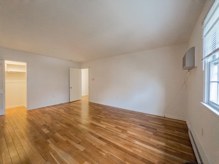Spacious, sunlit room with gleaming hardwood floors and a large window, perfect for comfortable living.