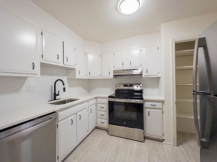 Contemporary kitchen with sleek stainless steel appliances, pristine white cabinetry, and elegant tile flooring.