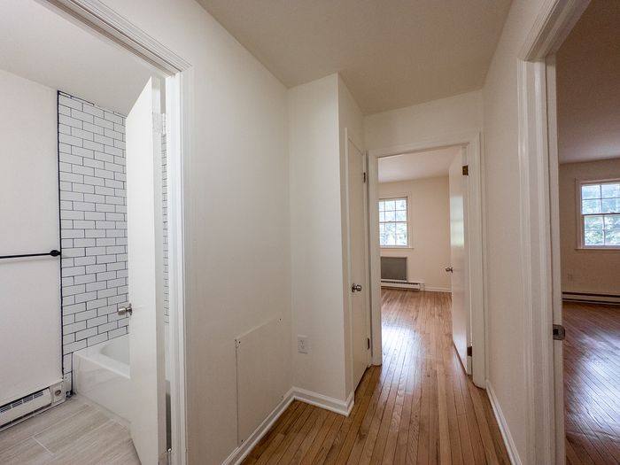 Inviting hallway view showcasing light-filled rooms with hardwood floors and modern tiled bathroom.