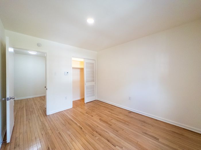 Bright and inviting empty room with natural wood flooring and ample closet space, perfect for personalization and modern living.