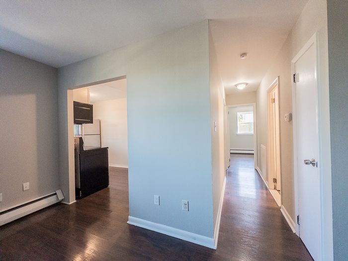 Inviting apartment hallway with dark hardwood floors, leading to a bright kitchen and cozy living space.