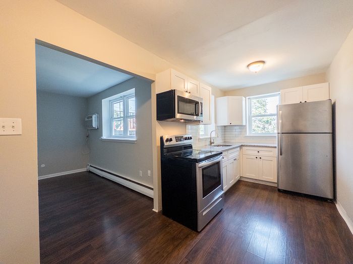 Modern kitchen with stainless steel appliances, sleek white cabinets, and rich hardwood floors, leading into a cozy adjacent room.