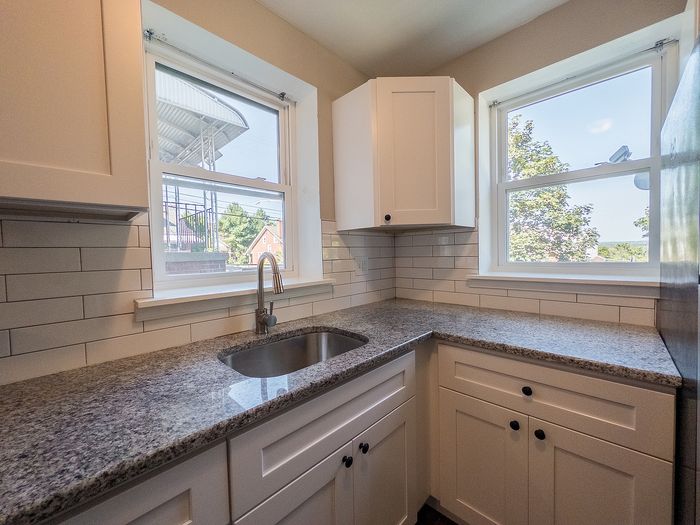 Bright and modern kitchen with granite countertops, white cabinets, and scenic views from two windows.