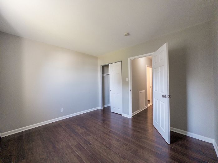 Bright, spacious room with elegant hardwood flooring and modern paint, featuring an open door leading to a hallway.