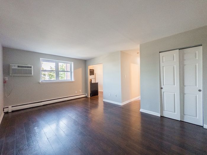 Bright, spacious living area with sleek hardwood floors, large window, and modern closet doors.