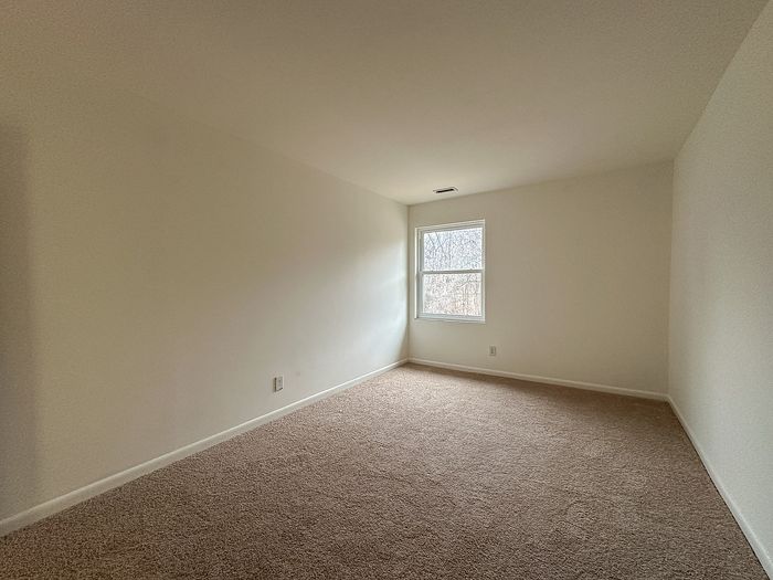 Bedroom with beige carpet and single window.