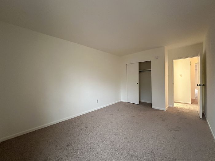Empty carpeted bedroom with window and open door at Woodcrest Village Apartments in Fairless Hills, PA.