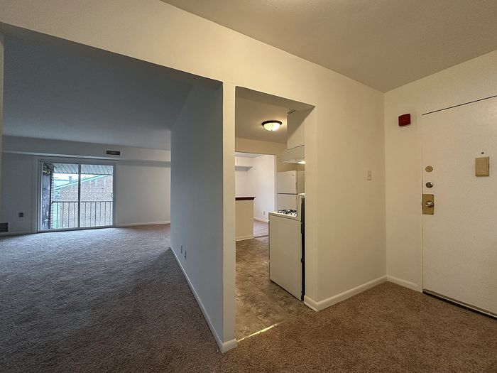 Woodcrest Village apartment entryway leading to kitchen and carpeted living room with sliding glass door to balcony.