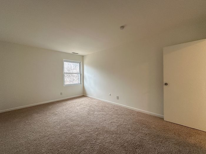 Empty carpeted bedroom with window and open door at Woodcrest Village Apartments in Fairless Hills, PA.
