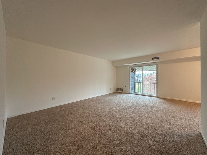 Spacious carpeted living room at Woodcrest Village Apartments with sliding glass door to balcony.