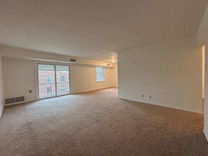 Empty carpeted living room with sliding glass door to balcony and a side window.