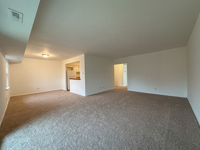 Open living room with carpet, pass-through kitchen, and neutral walls.