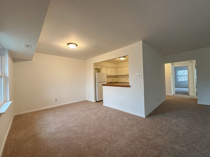 Carpeted living room with pass-through counter to kitchen at Woodcrest Village Apartments