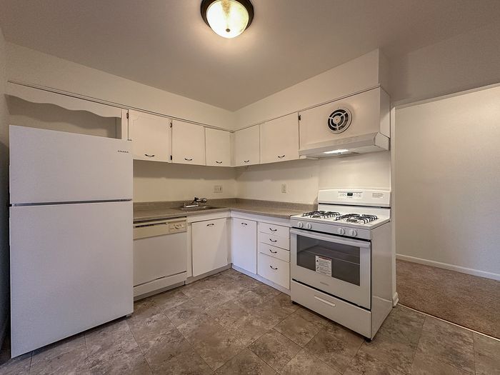 Kitchen with white appliances, white cabinetry and laminate floors at Woodcrest Village Apartments