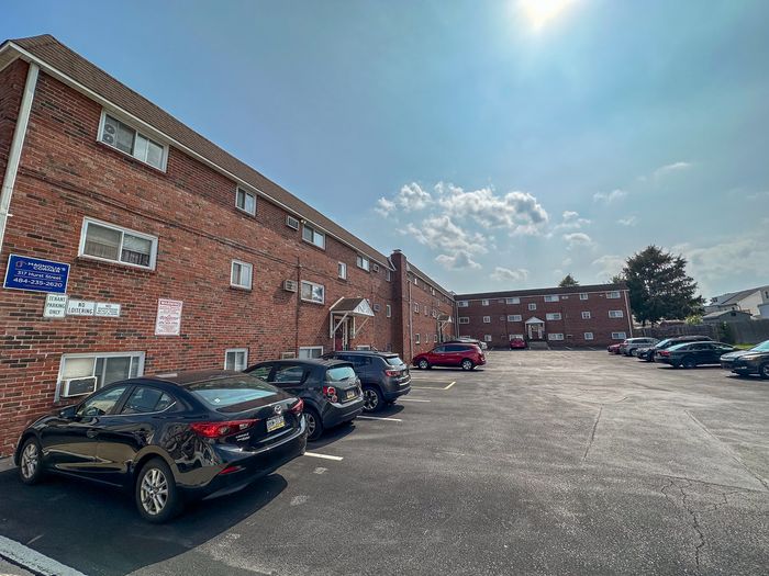 Charming brick apartment building with ample parking space under a bright blue sky, perfect for modern living.