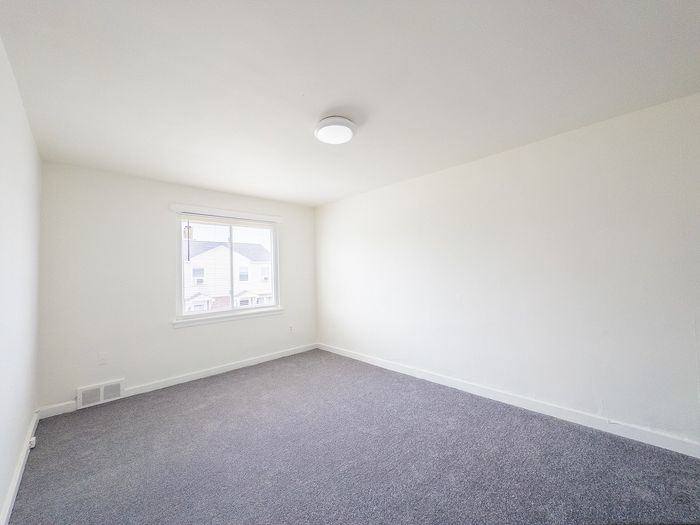 Bright, spacious room with plush gray carpeting and a large window inviting natural light.