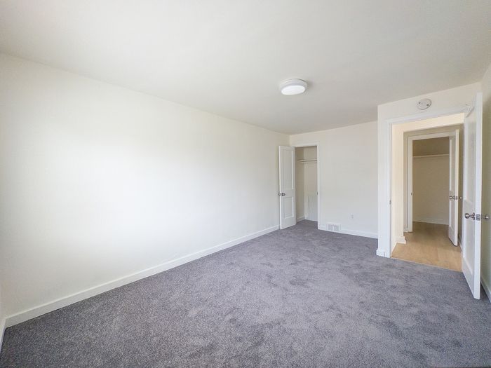 Bright and spacious bedroom with plush carpeting and a modern closet, perfect for relaxation and comfort.