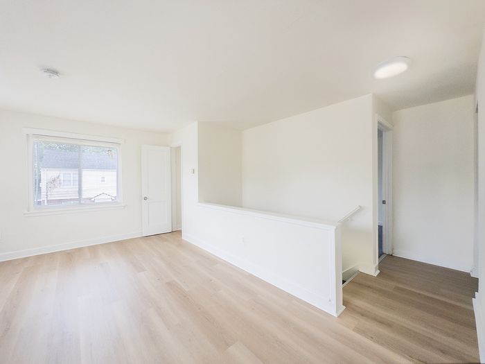 Bright and spacious room with sleek wooden flooring, abundant natural light from large window, and elegant white walls.