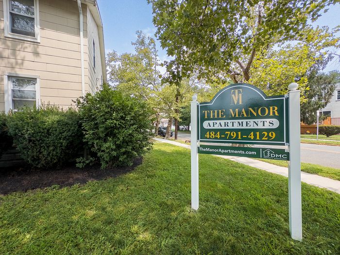 Charming exterior view of The Manor Apartments with lush greenery, offering premium living spaces in a serene neighborhood.