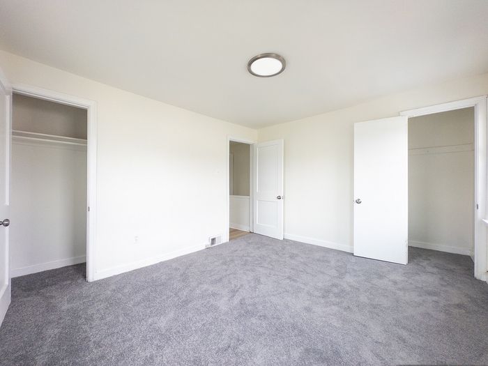 Bright and spacious bedroom with fresh white walls, plush gray carpeting, and ample closet space.