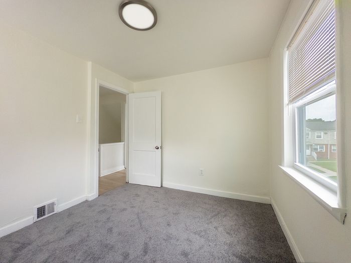 Bright and airy room with plush carpet and large window showcasing a charming neighborhood view.