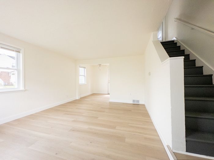 Bright and airy living space with elegant hardwood floors and a modern staircase, perfect for stylish urban living.