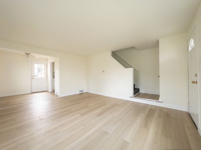 Bright and spacious living area with elegant wooden flooring and natural light, featuring access to a staircase and adjoining rooms.