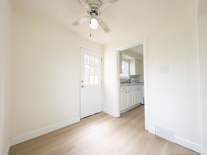 Bright, spacious kitchen entrance with elegant double doors and sleek hardwood flooring, leading into a modern white kitchen area.
