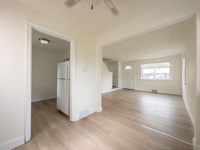 Bright and airy open-plan living area with modern wooden flooring and large windows, leading to a cozy kitchen space.