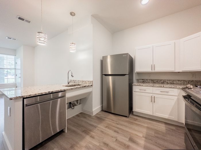 Modern kitchen design featuring stainless steel appliances, elegant granite countertops, and sleek white cabinetry, illuminated by stylish pendant lighting.