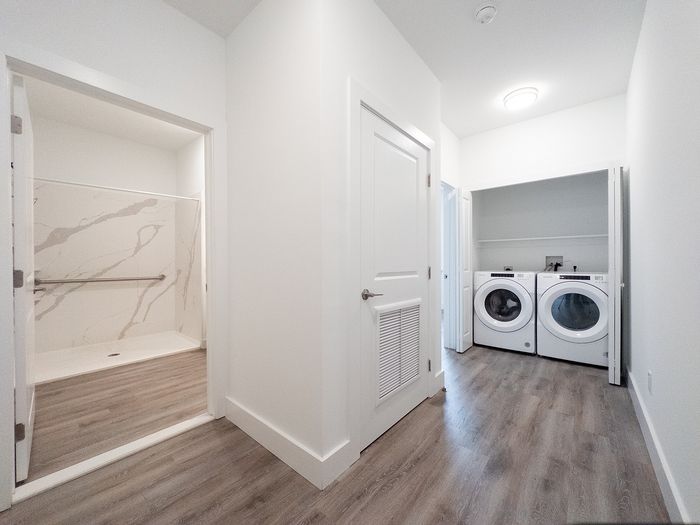 Modern apartment hallway featuring sleek wood flooring, elegant marble-tiled bathroom, and convenient in-unit laundry facilities.