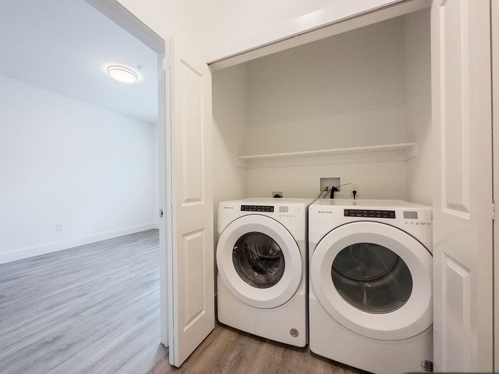 Modern apartment showcasing a convenient in-unit laundry with sleek washer and dryer, adjacent to a spacious, light-filled room with elegant flooring.