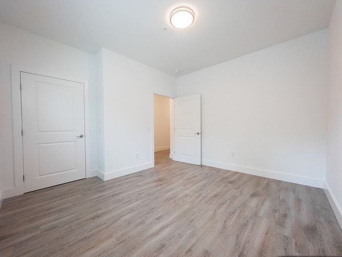 Spacious bedroom with modern wood flooring and bright natural light, ready for personal touch.