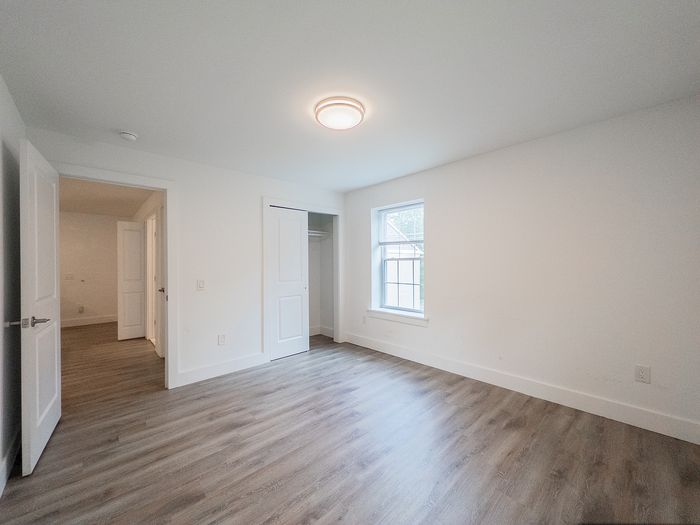 Bright and spacious bedroom with modern hardwood flooring, large window, and ample closet space, offering a versatile canvas for personalization.